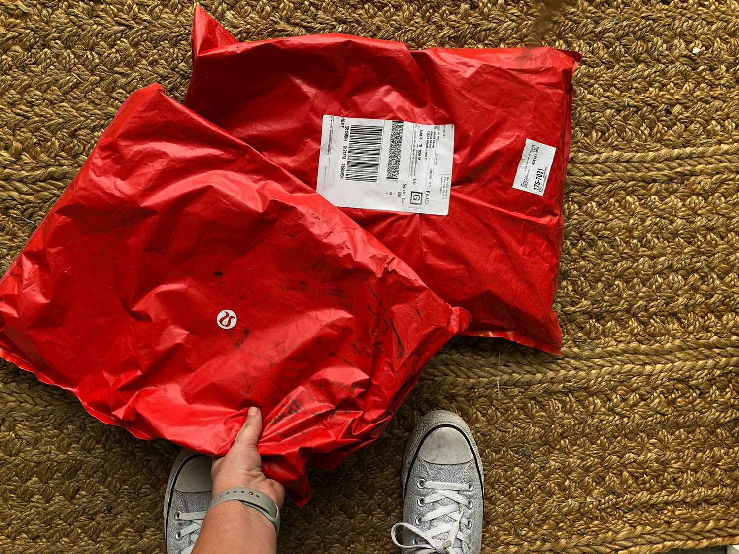 A person picking up one of two Lululemon packages on their front door mat.