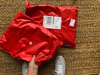 A person picking up one of two Lululemon packages on their front door mat.