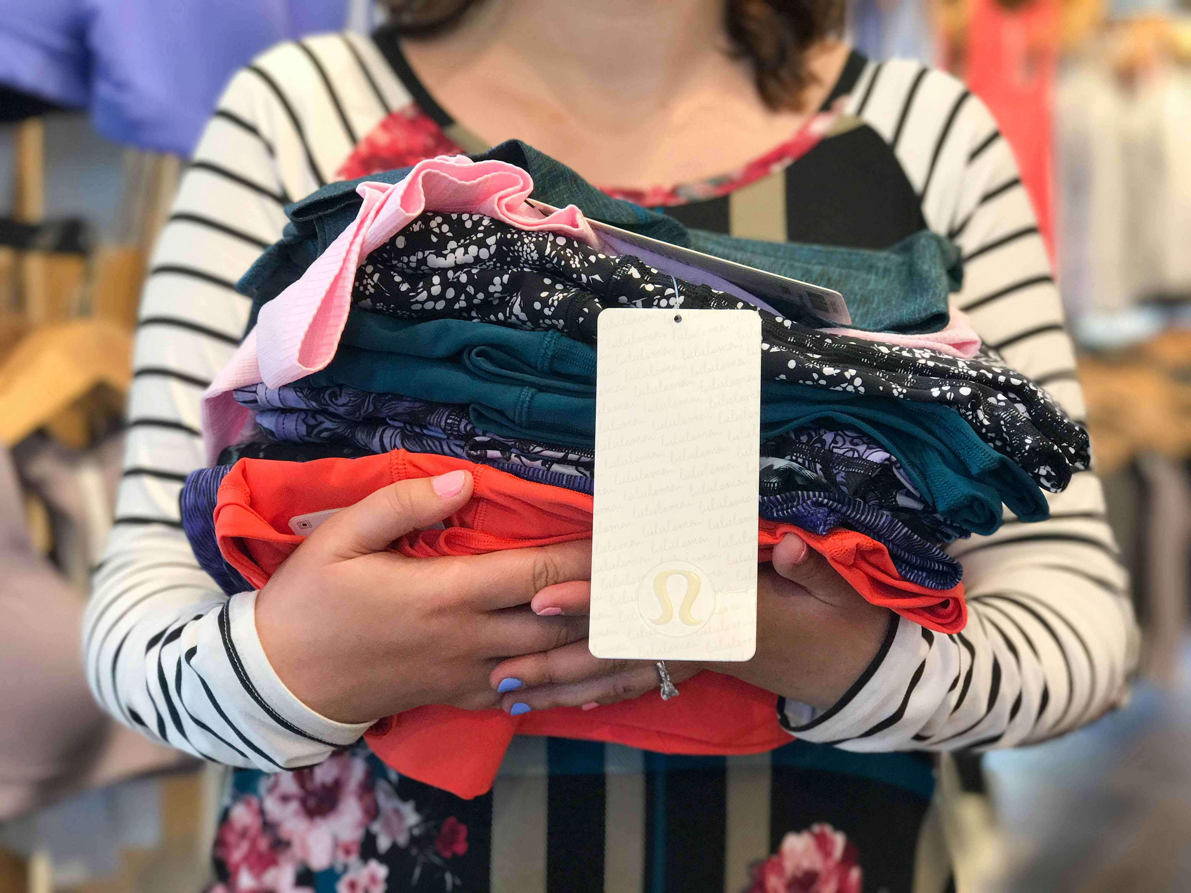 A person holding a pile of Lululemon clothing with a tag hanging down with the logo.