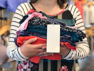A person holding a pile of Lululemon clothing with a tag hanging down with the logo.