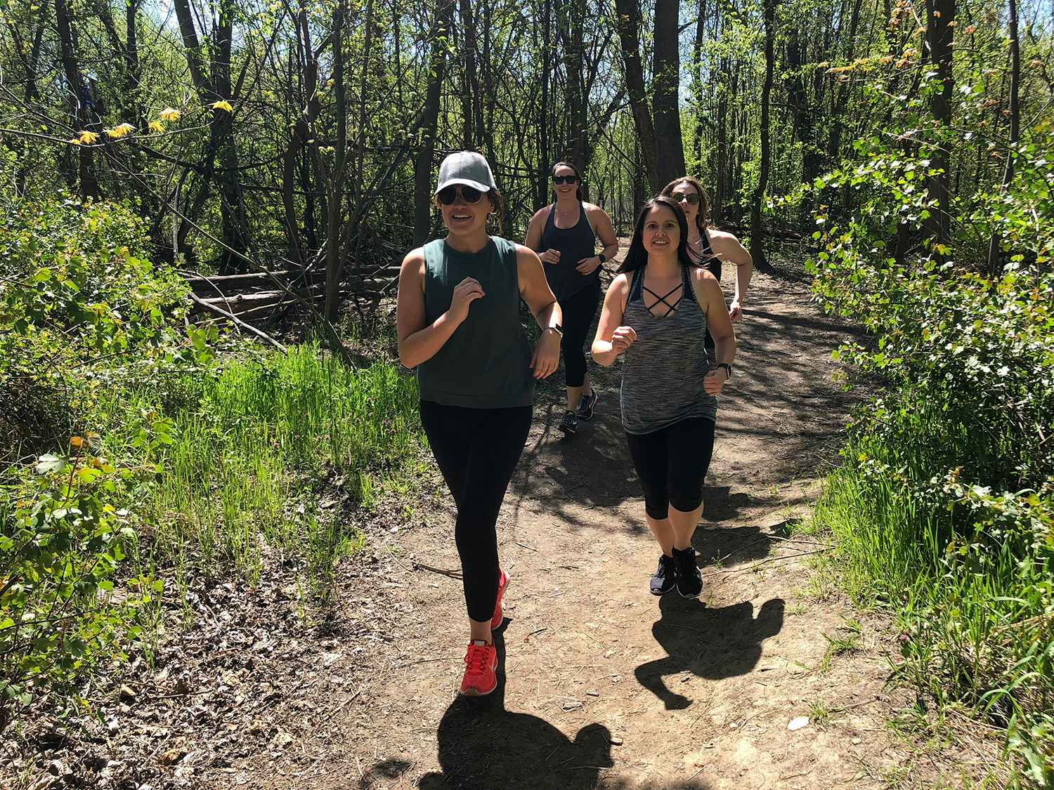 Some women running together on a path through some woods.