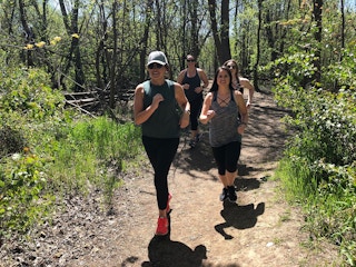 Some women running together on a path through some woods.
