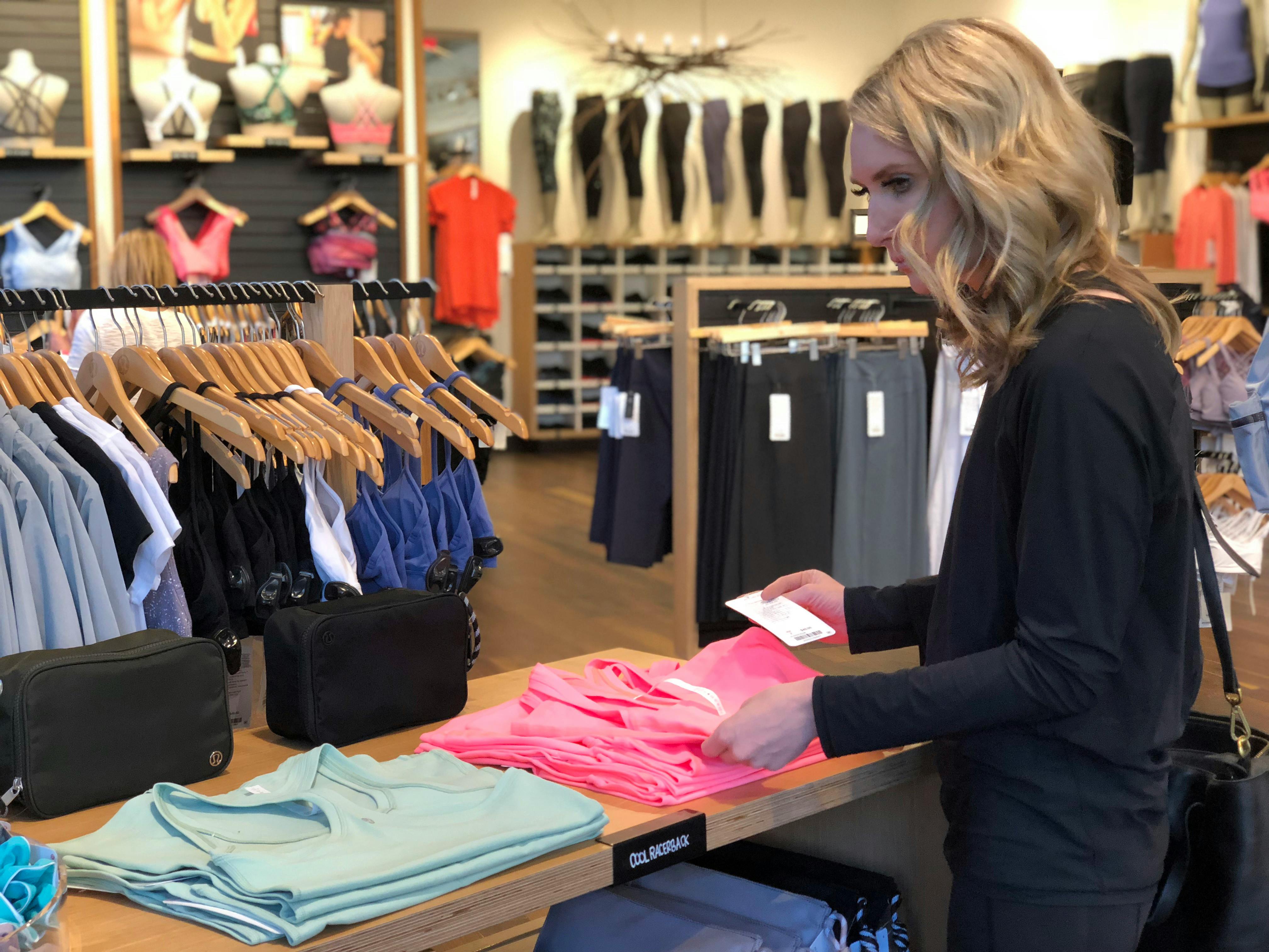 A woman looking at folded tank tops on a table at a lululemon store
