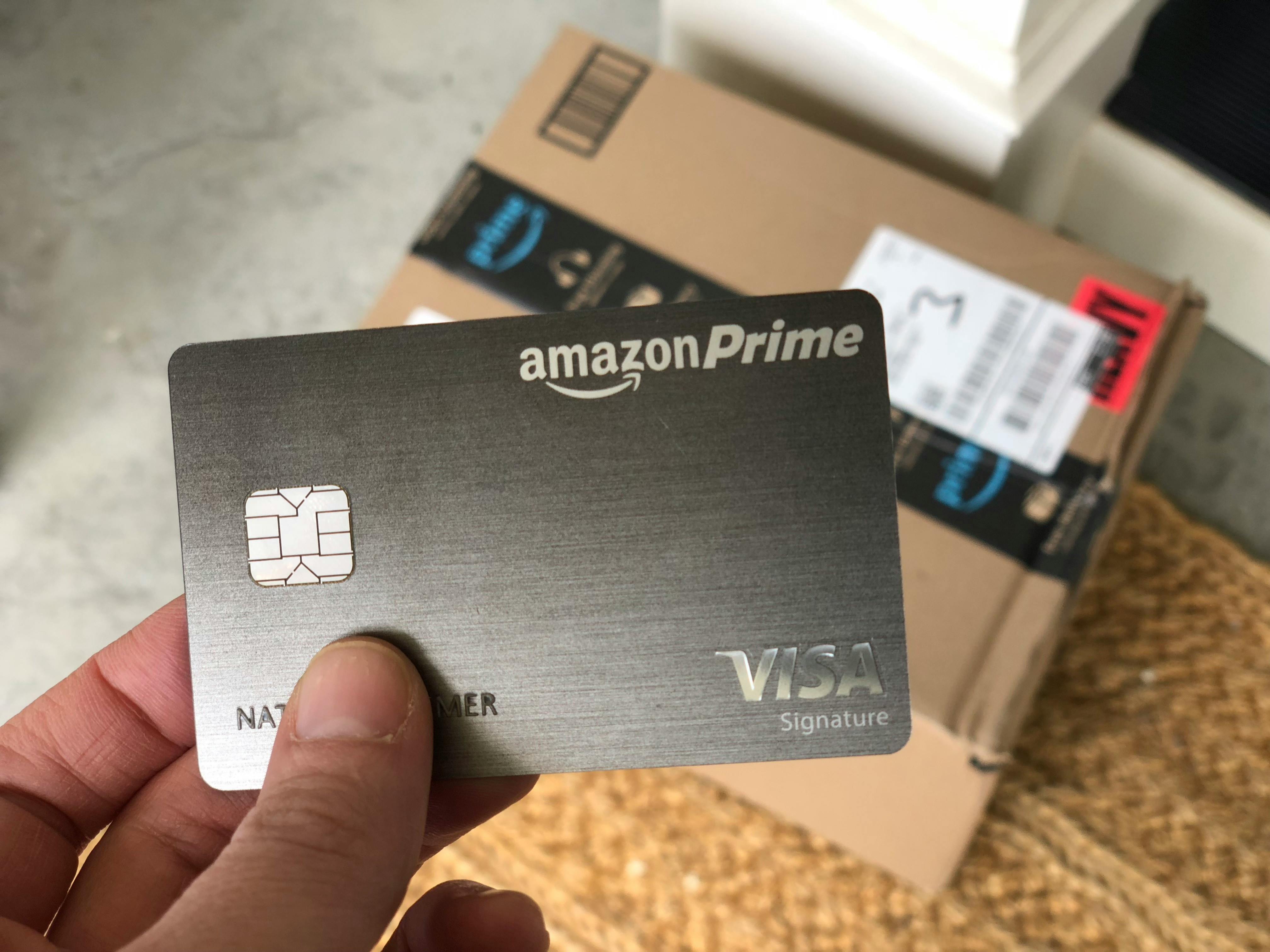 An Amazon Prime credit card held with an Amazon box on a doorstep in the background