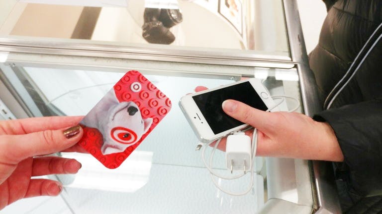Two people's hands, one holding up an iPhone and charger, and the other holding up a Target gift card to trade.