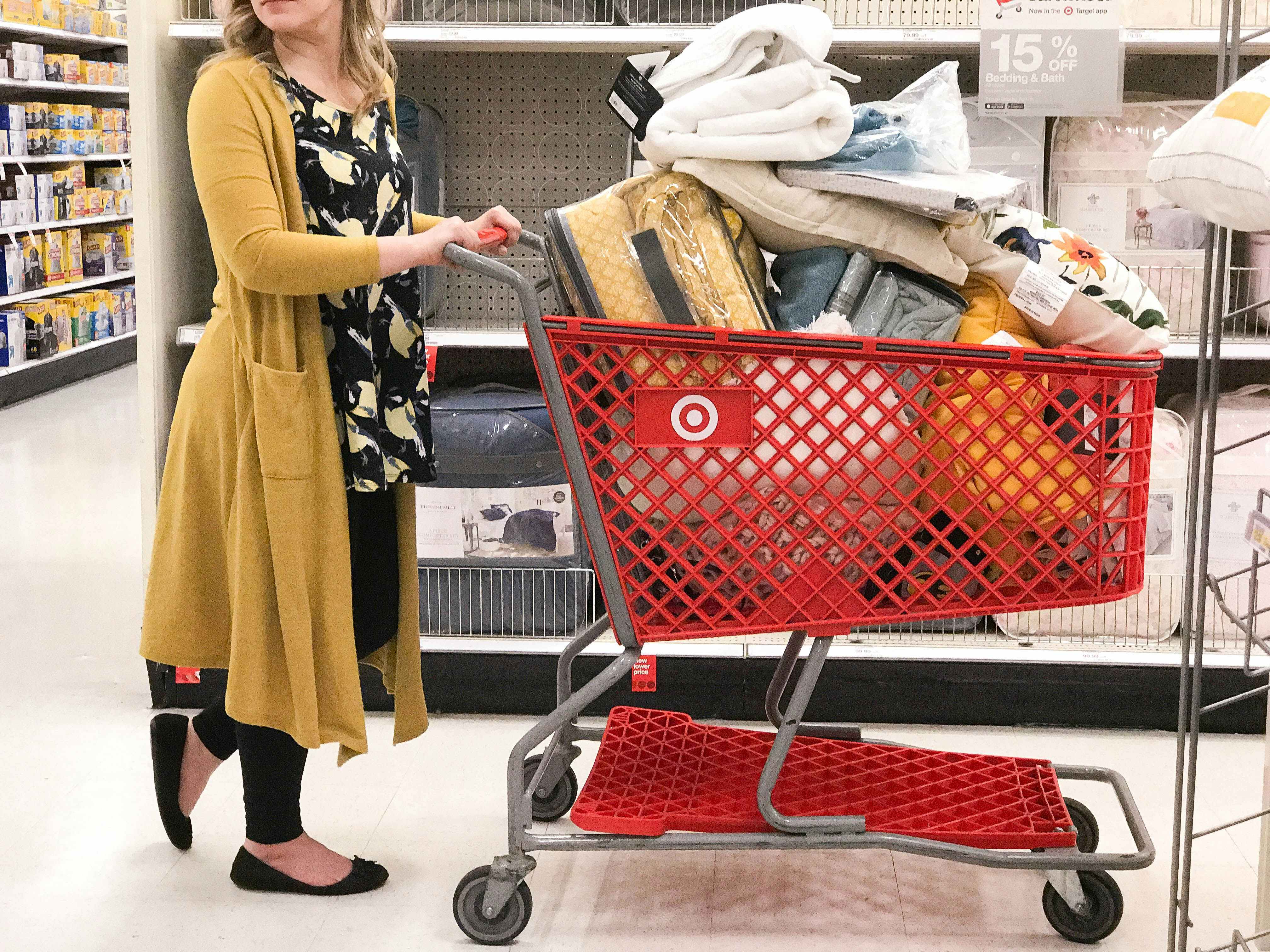 A woman pushing a target shipping car filled with bedding, towels and home items.