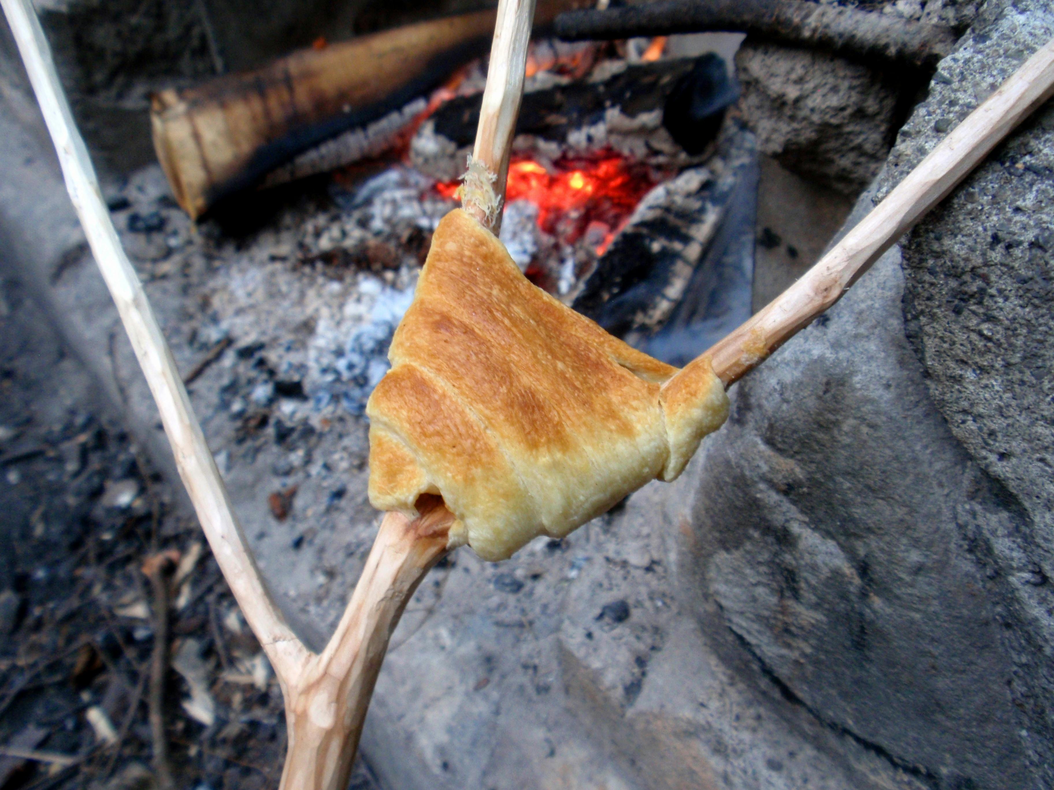 A stick with a crescent roll being held over a fire pit.
