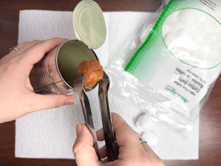 Someone dipping cotton balls into melted wax in a can