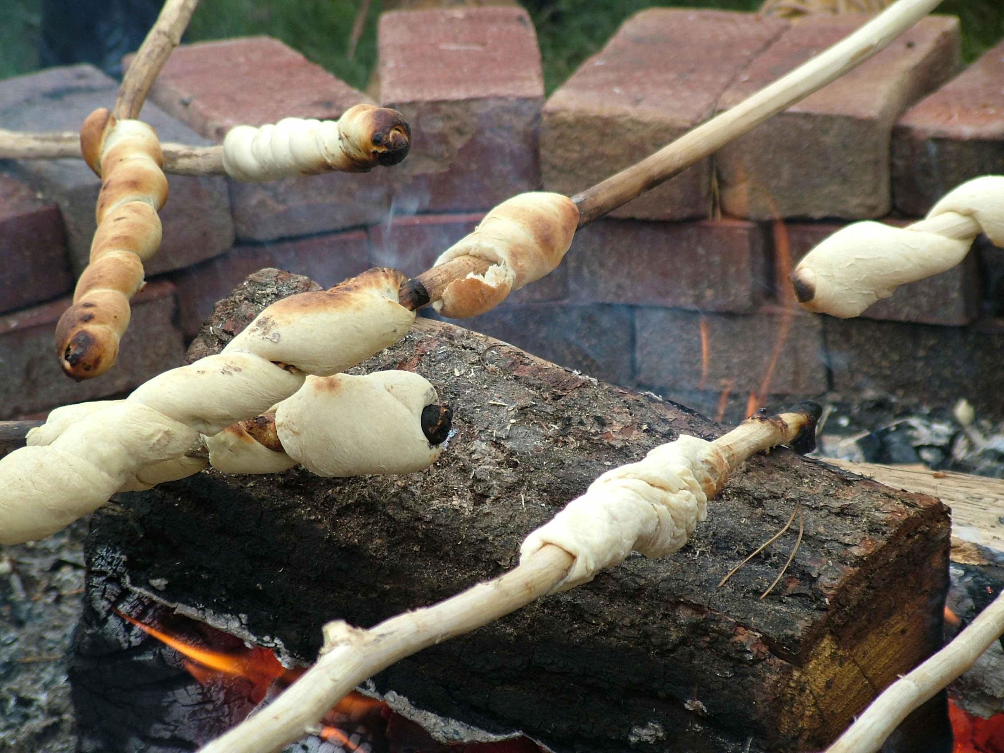 A bunch of people cooking some crescent rolls on a campfire