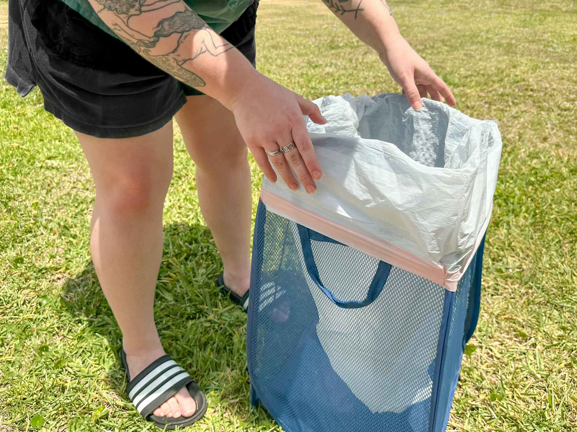 Someone putting a trash bag into a foldable laundry basket to use it as a trash can while camping