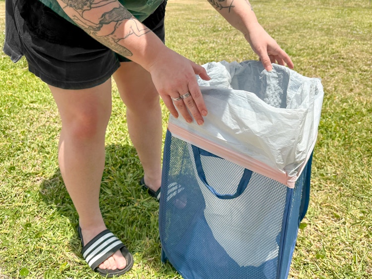 Someone putting a trash bag into a foldable laundry basket to use it as a trash can while camping