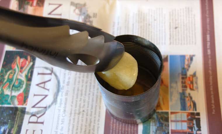 Someone using tongs to dip a cotton ball into some melted wax in a can.