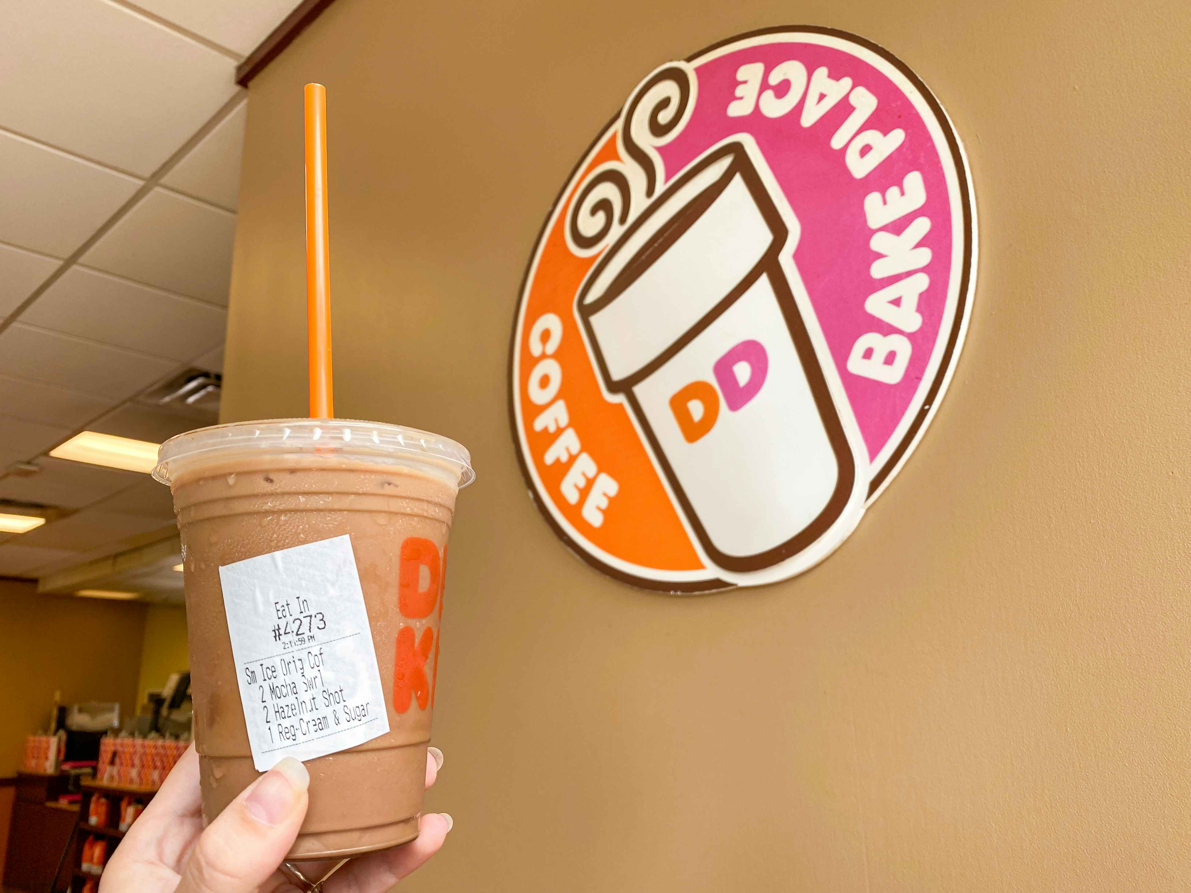 hand holding specialty iced coffee near Dunkin sign inside restaurant
