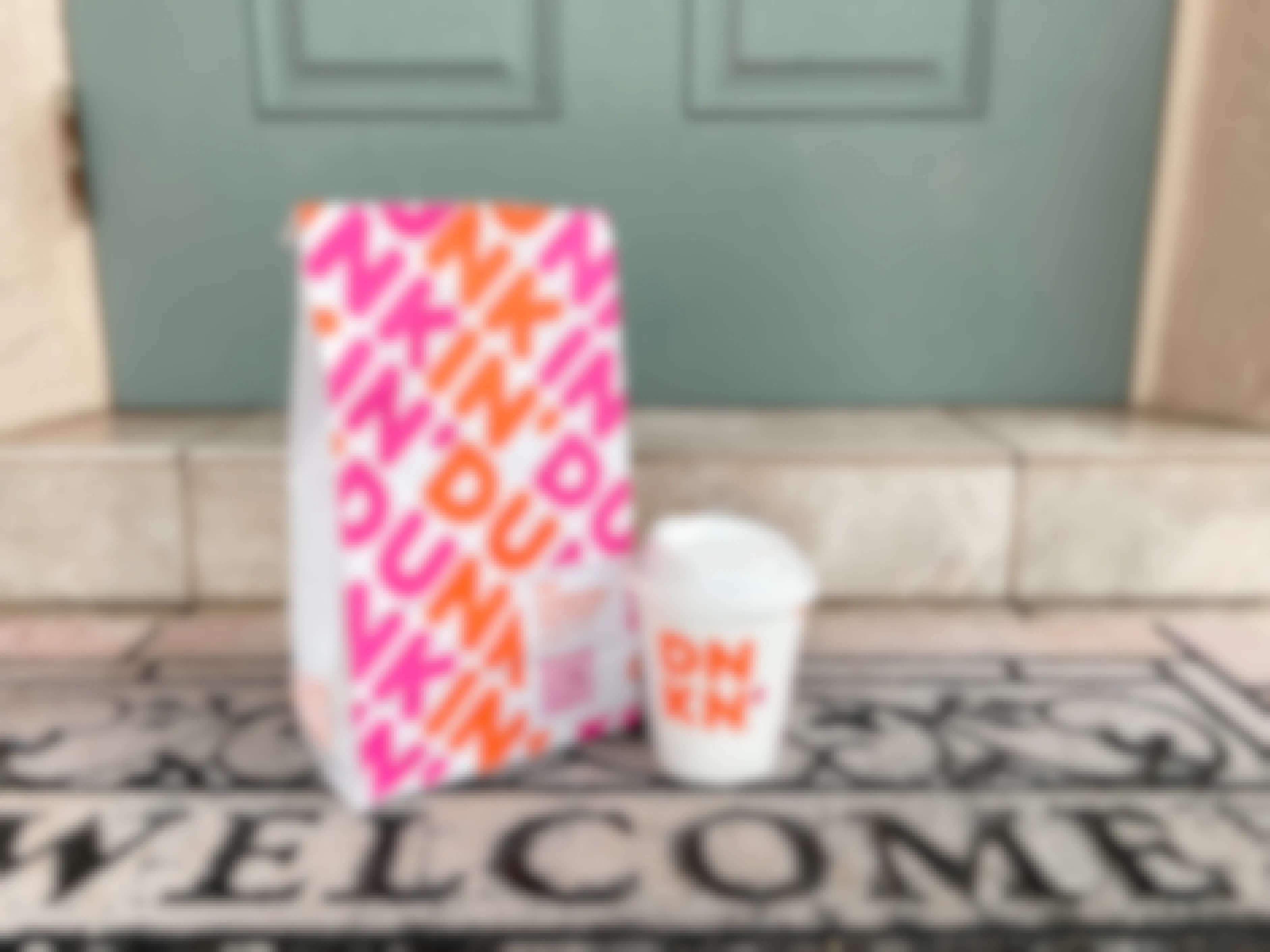 dunkin takeout bag and small coffee on front porch welcome mat