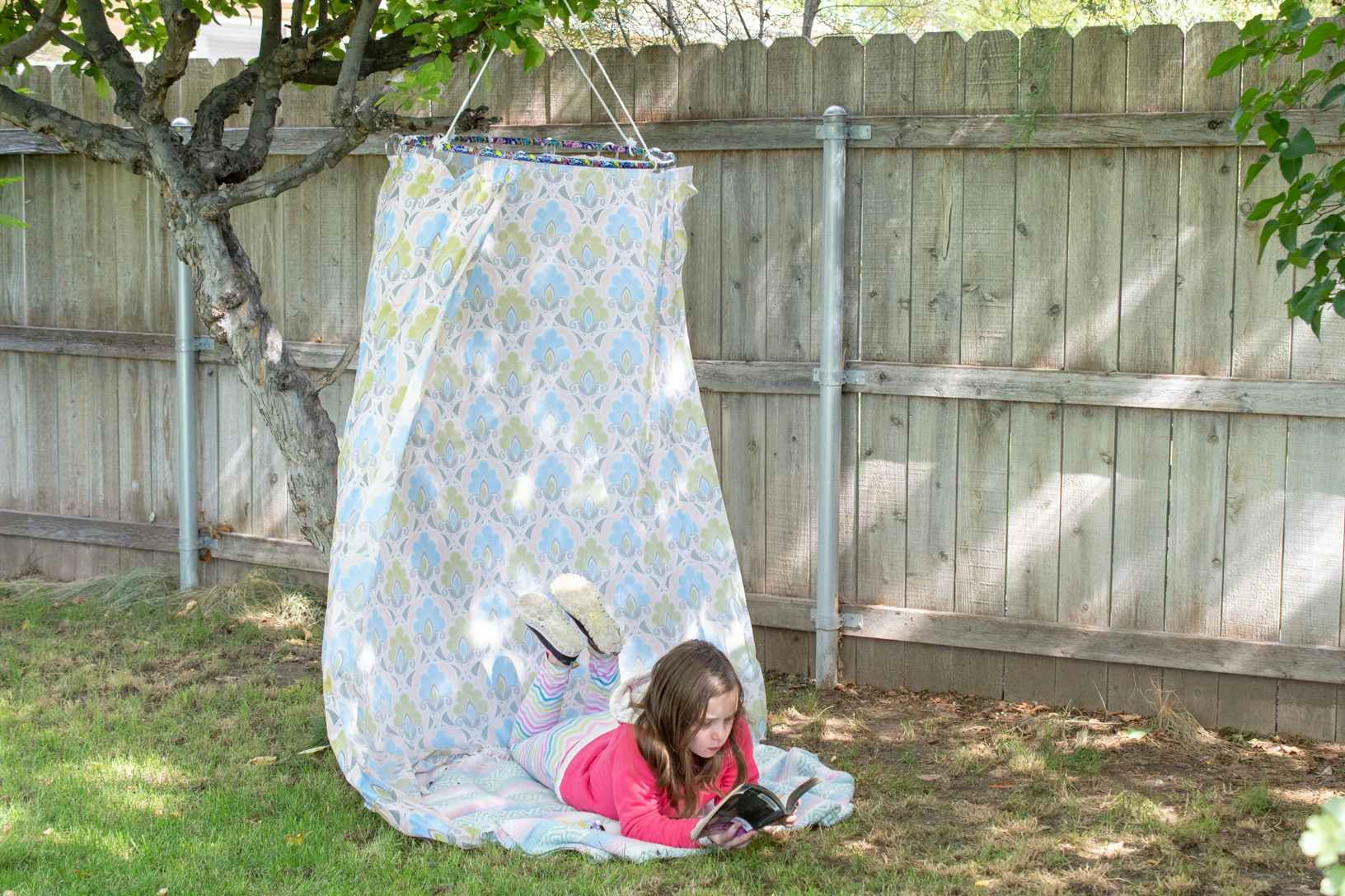 A child reading a book while laying on a DIY hideout set up in a backyard.