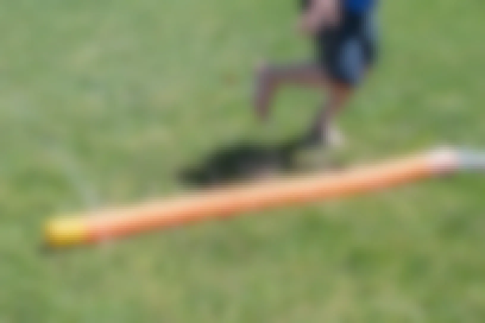 A child playing around a DIY pool noodle sprinkler that is attached to a hose on a lawn.