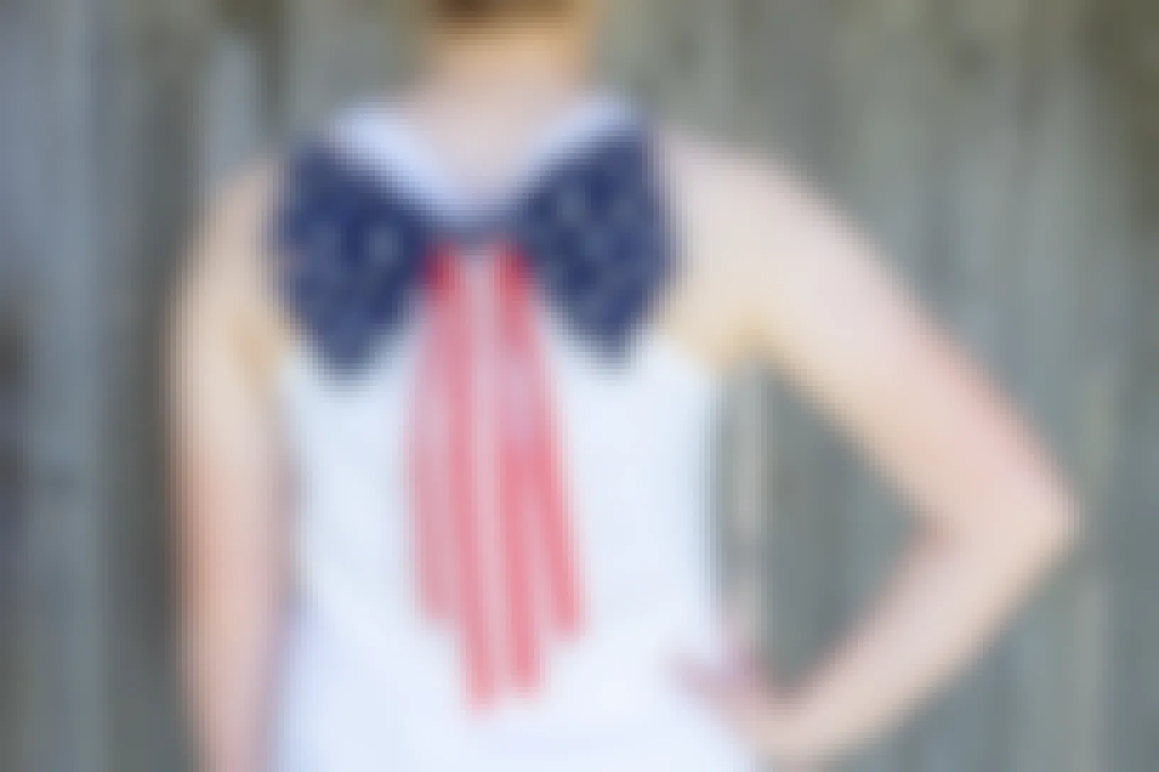 A decorative American flag bow attached to the back of a person's white tank top, standing facing away toward a fence.