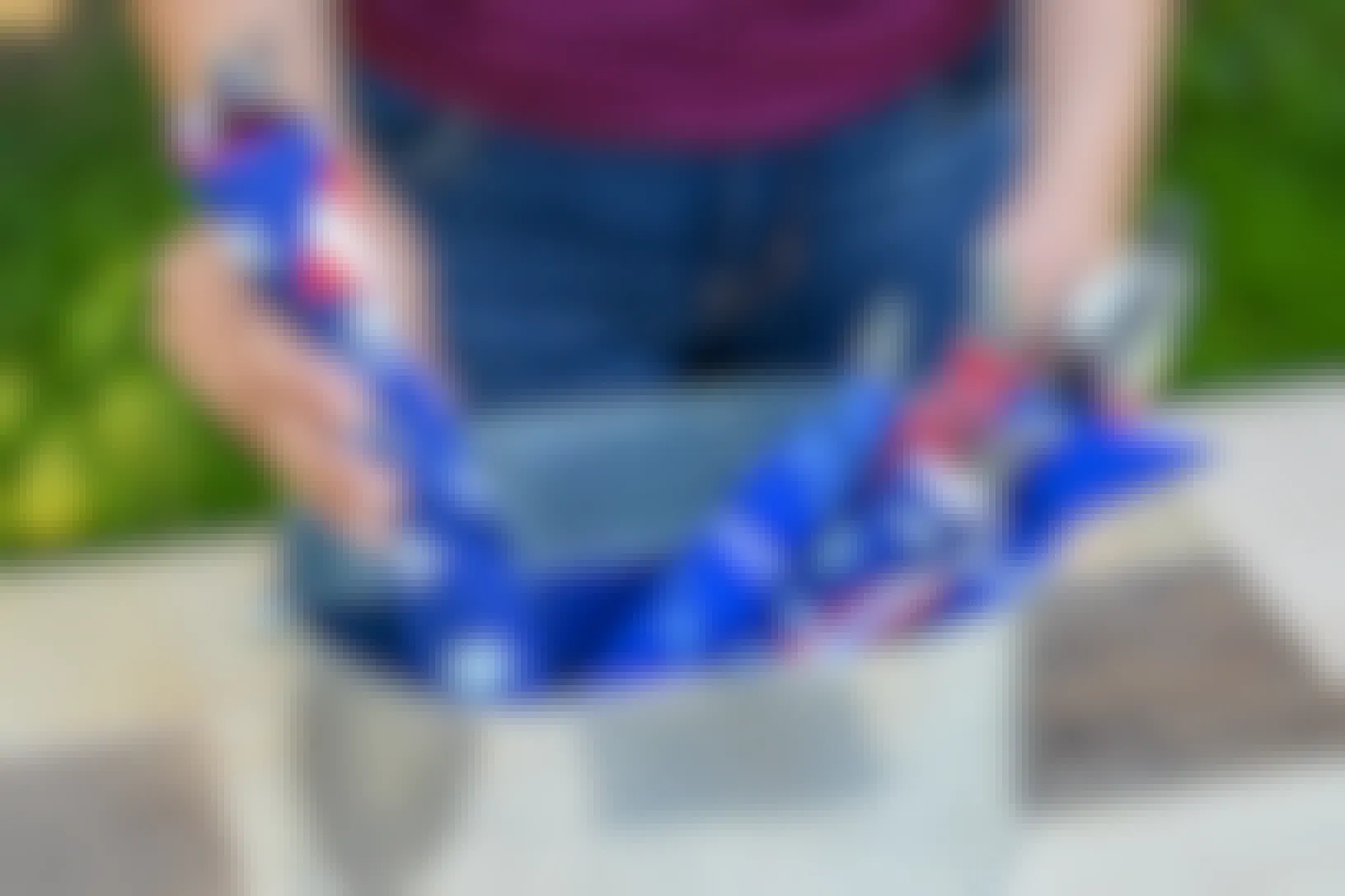 A person putting a set of silverware wrapped in a red, white, and blue bandana into a container with similarly wrapped silverware sets.