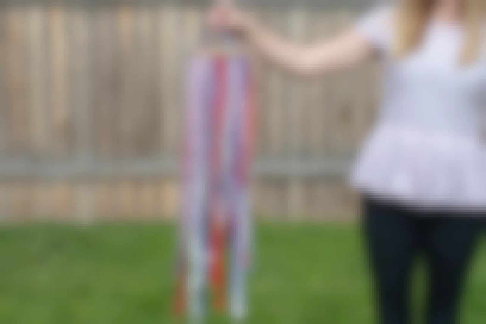 A person standing in a backyard, holding up a DIY windsock made of ribbon and an embroidery hoop.