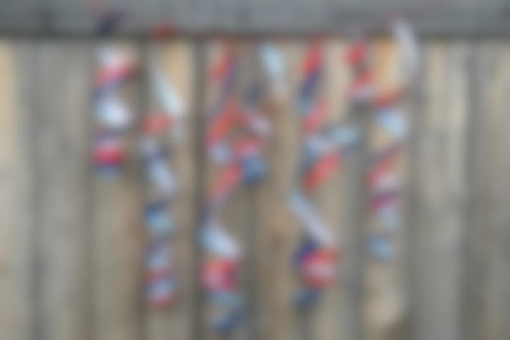 Twirly streamers hung together as a banner made from spiral-cut red and blue plastic cups, hanging on a wooden fence.