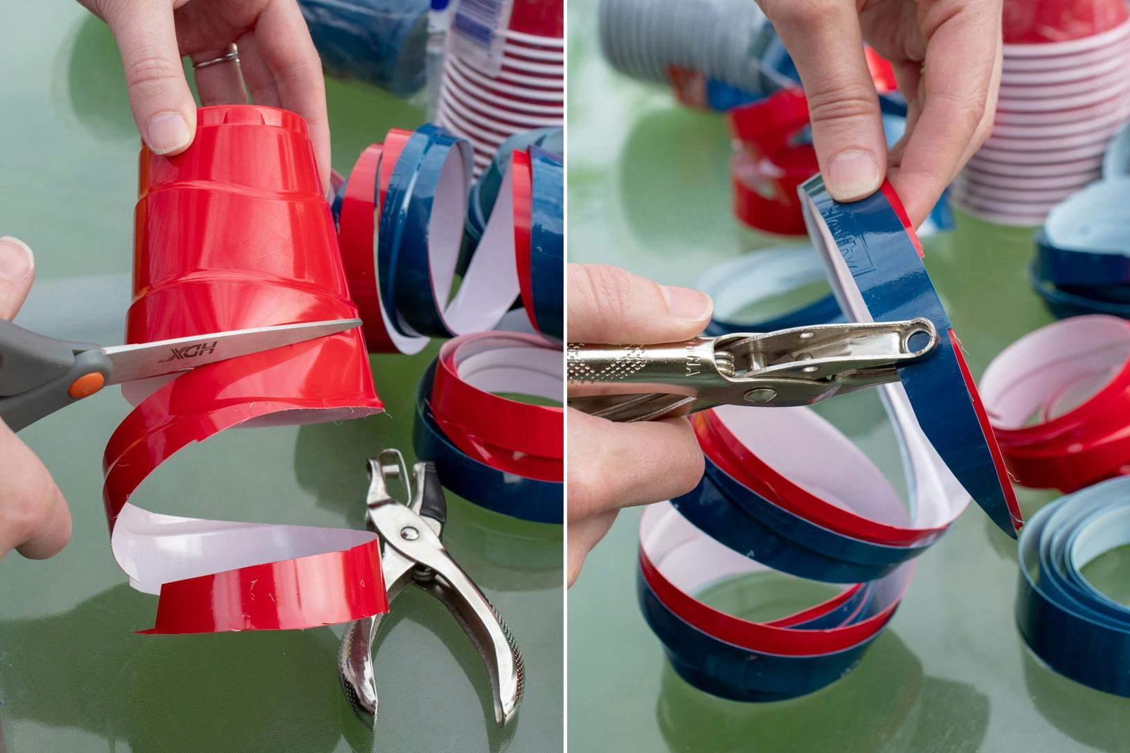 A person's hand cutting a red plastic cup in a spiral pattern to make twirly streamers, and punching a hole through the end to string multiple together.