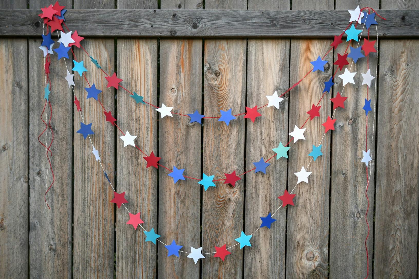 A DIY red, white, and blue star garland hanging from a wooden fence.