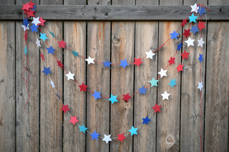 A DIY red, white, and blue star garland hanging from a wooden fence.