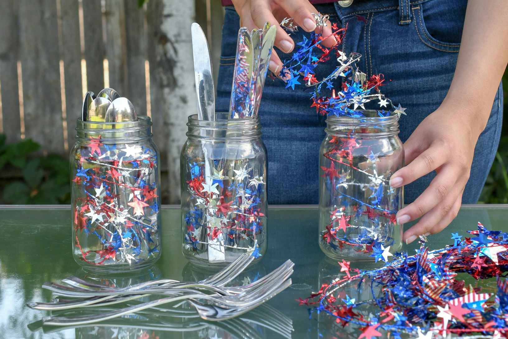 A person putting red, white, and blue spiral garland into mason jars for a decorative place for silverware.