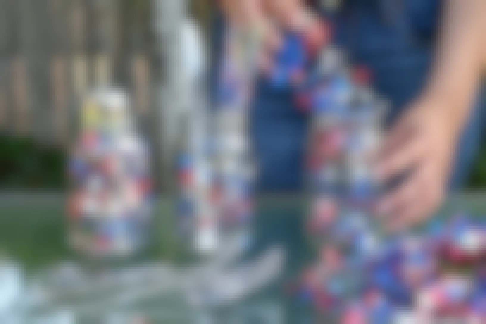 A person putting red, white, and blue spiral garland into mason jars for a decorative place for silverware.
