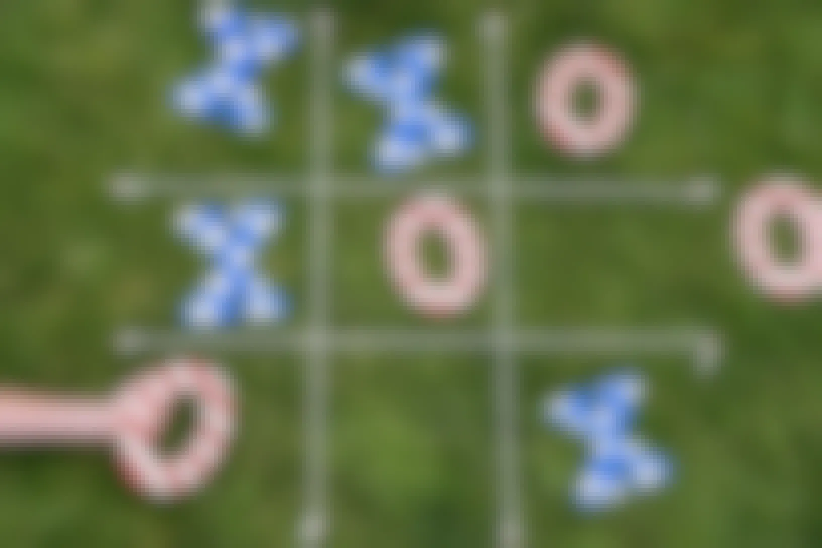A person placing a red-and-white-striped O in a space below a blue X with white stars on a lawn tic-tac-toe game.