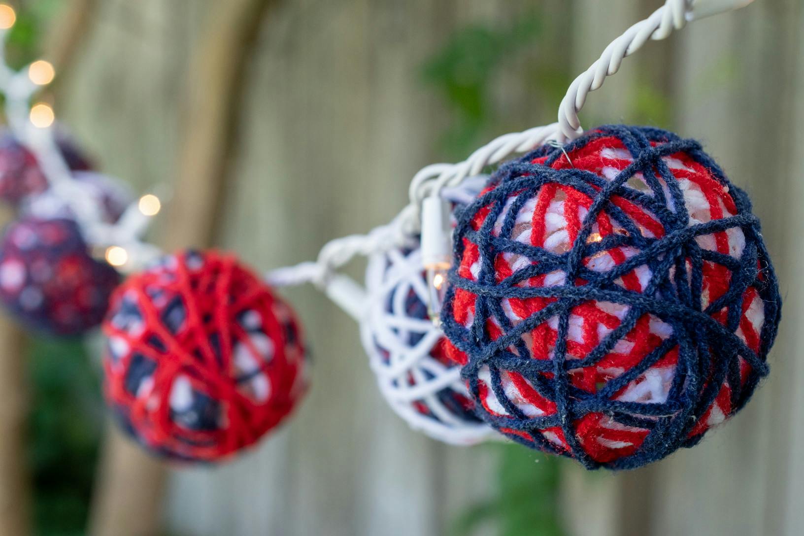 A string of DIY yarn ball lights hanging on a wooden fence.