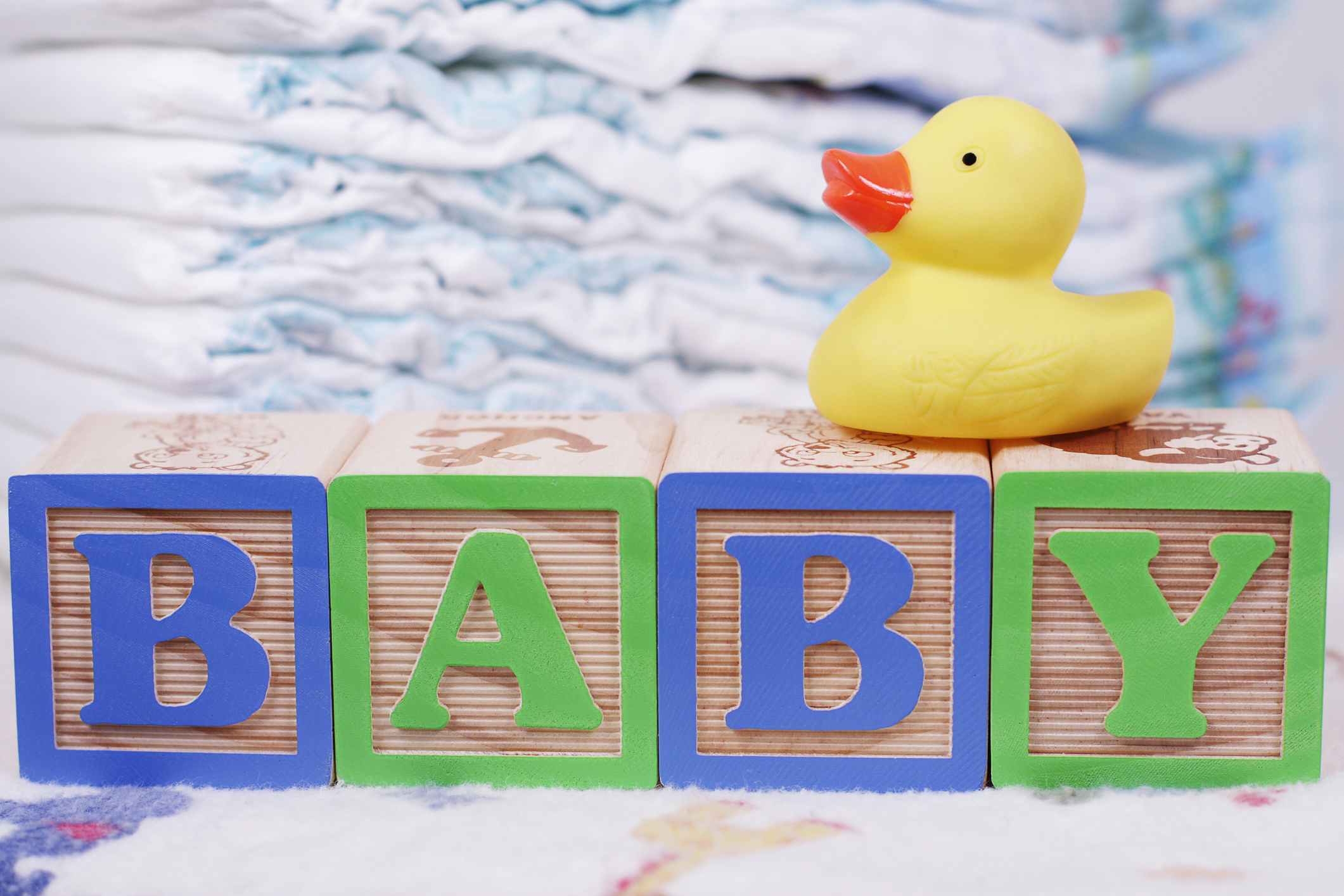 Some baby blocks arranged to spell the word "BABY" with a rubber duck on top and stacks of diapers in the background.