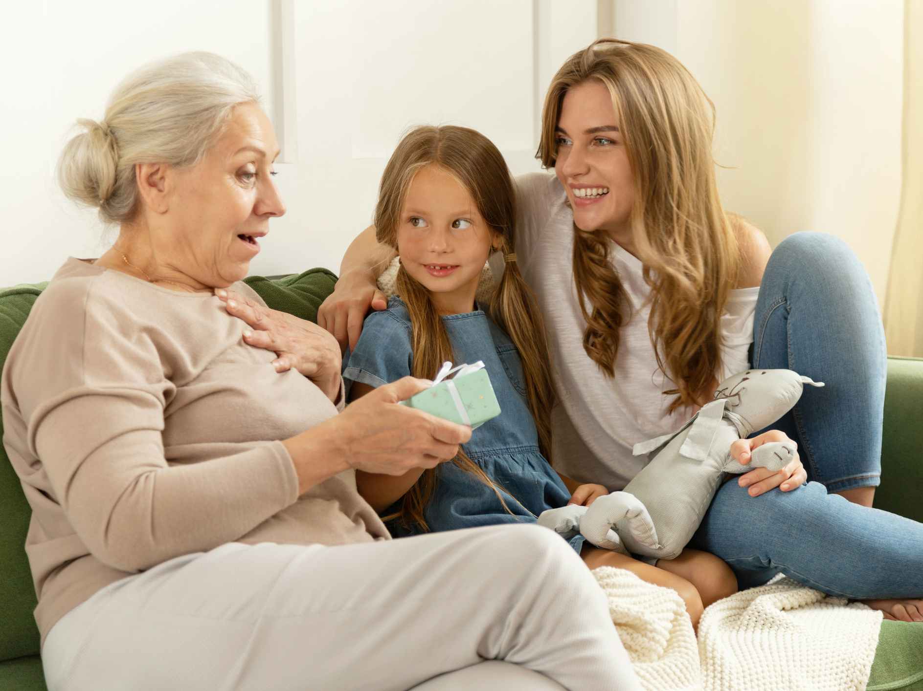 A grandmother opening a gift and looking surprised while her daughter and grand daughter watch and smile