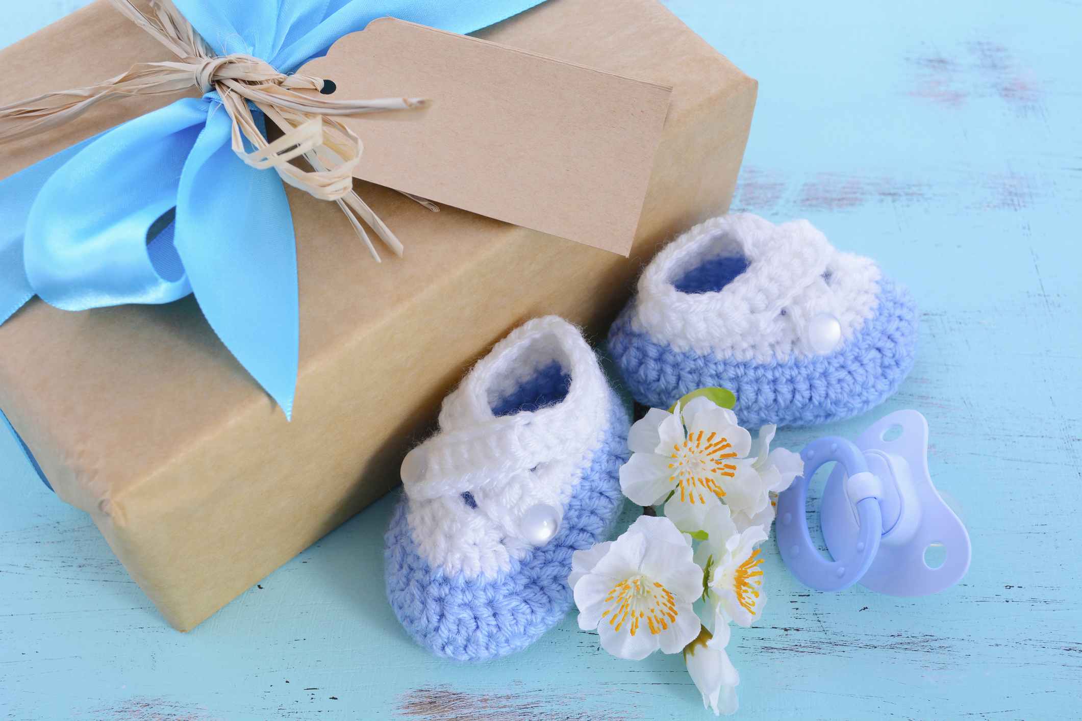 A baby gift box with a bow next to some booties and a pacifier on a table.