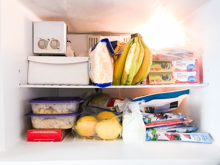 A freezer filled with foods like, lemons, bananas, cheese, and butter.