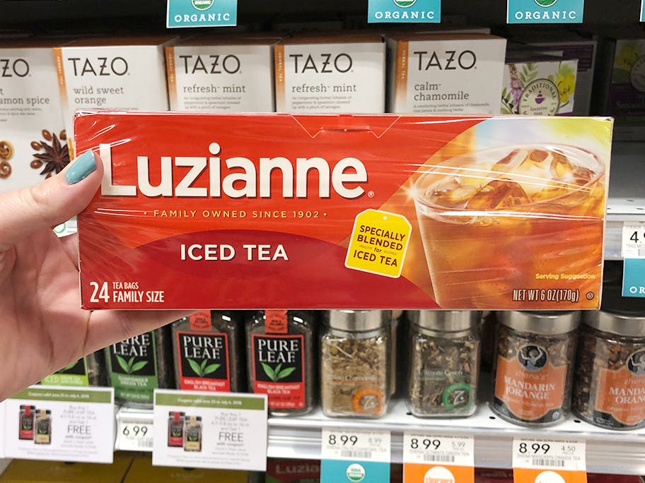 Someone holding up a box of Luzianne tea in front of a shelf of tea products at Publix