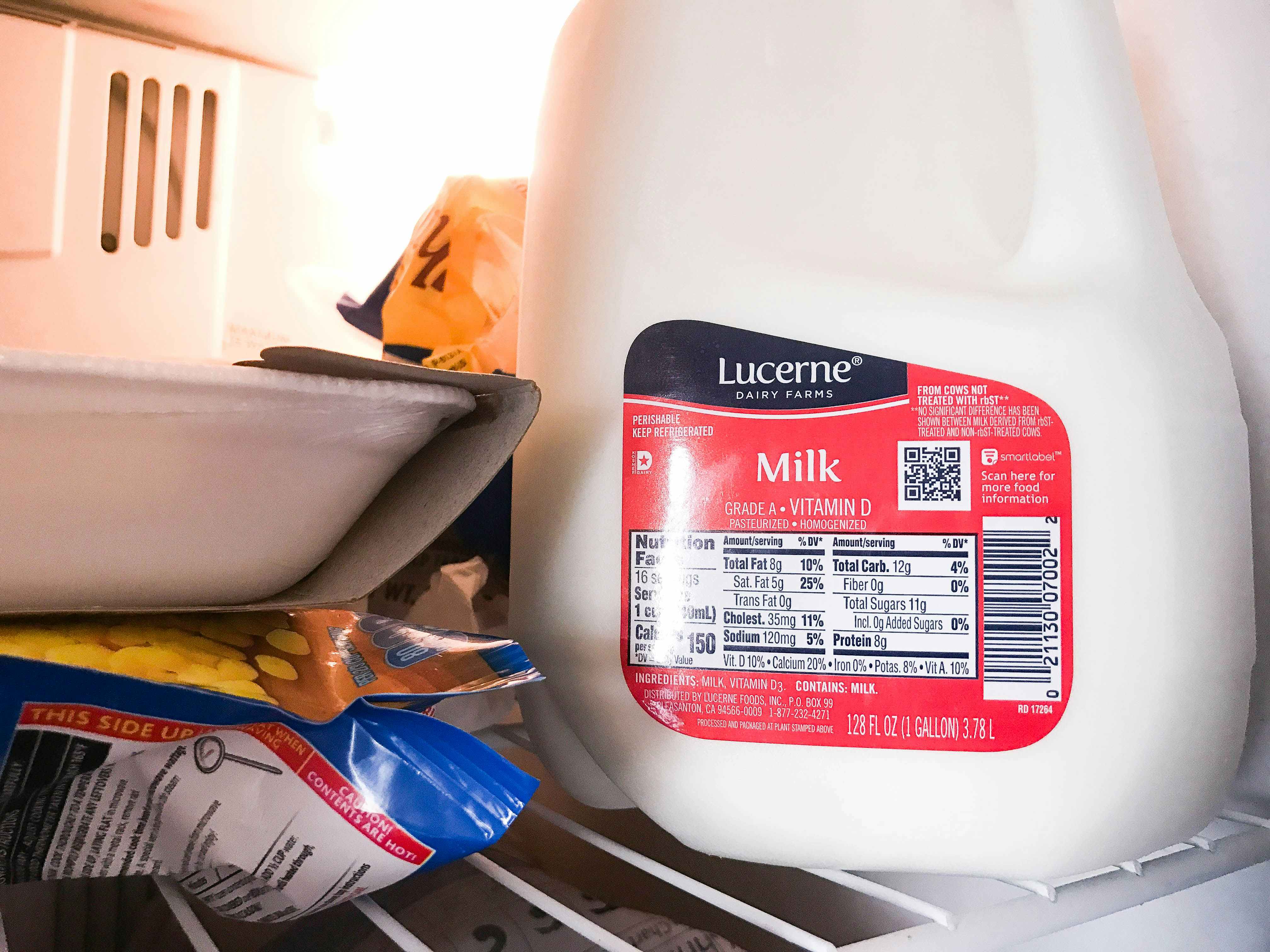A gallon of milk in a freezer next to other items.