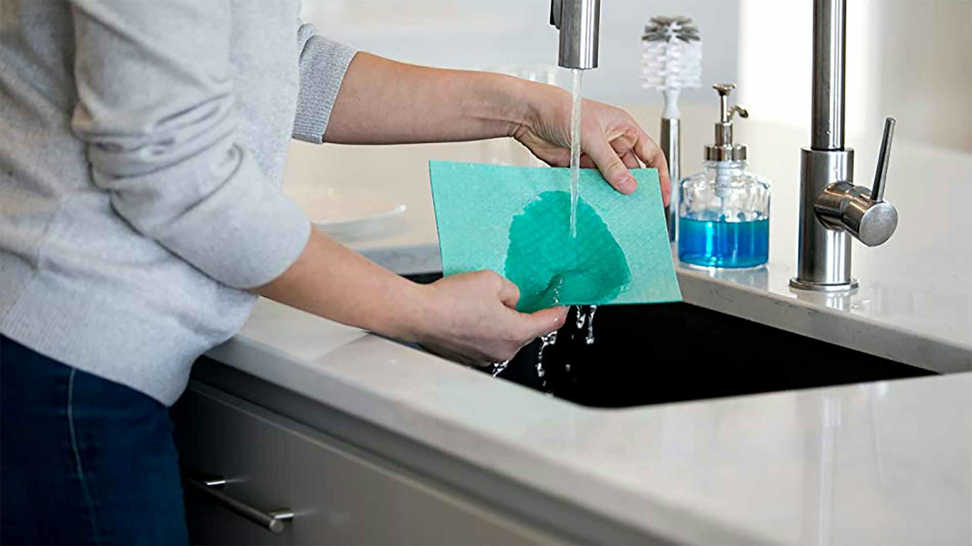 A woman rinsing a dish cloth under a kitchen faucet