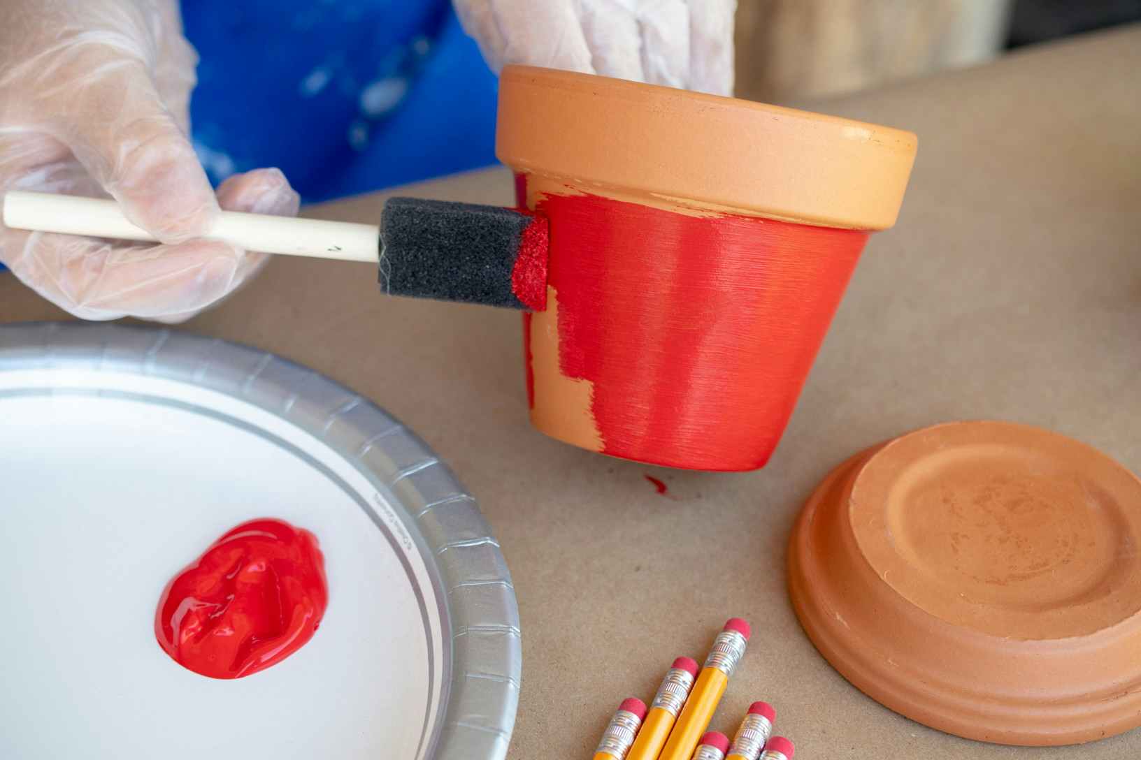 Woman using a sponge paint brush to paint a brown terracotta pot red.