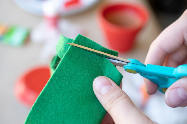 Woman cutting green felt with scissors.