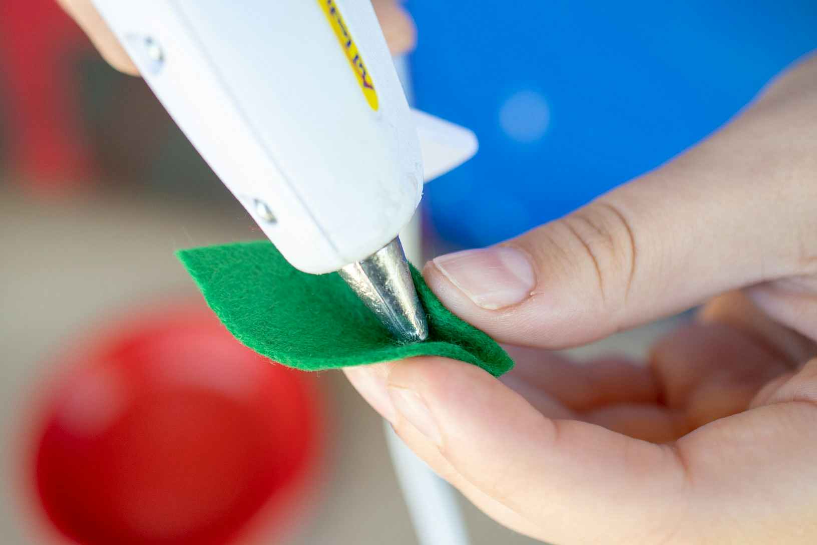 Woman pinching green felt and using hot glue to keep fold in place.