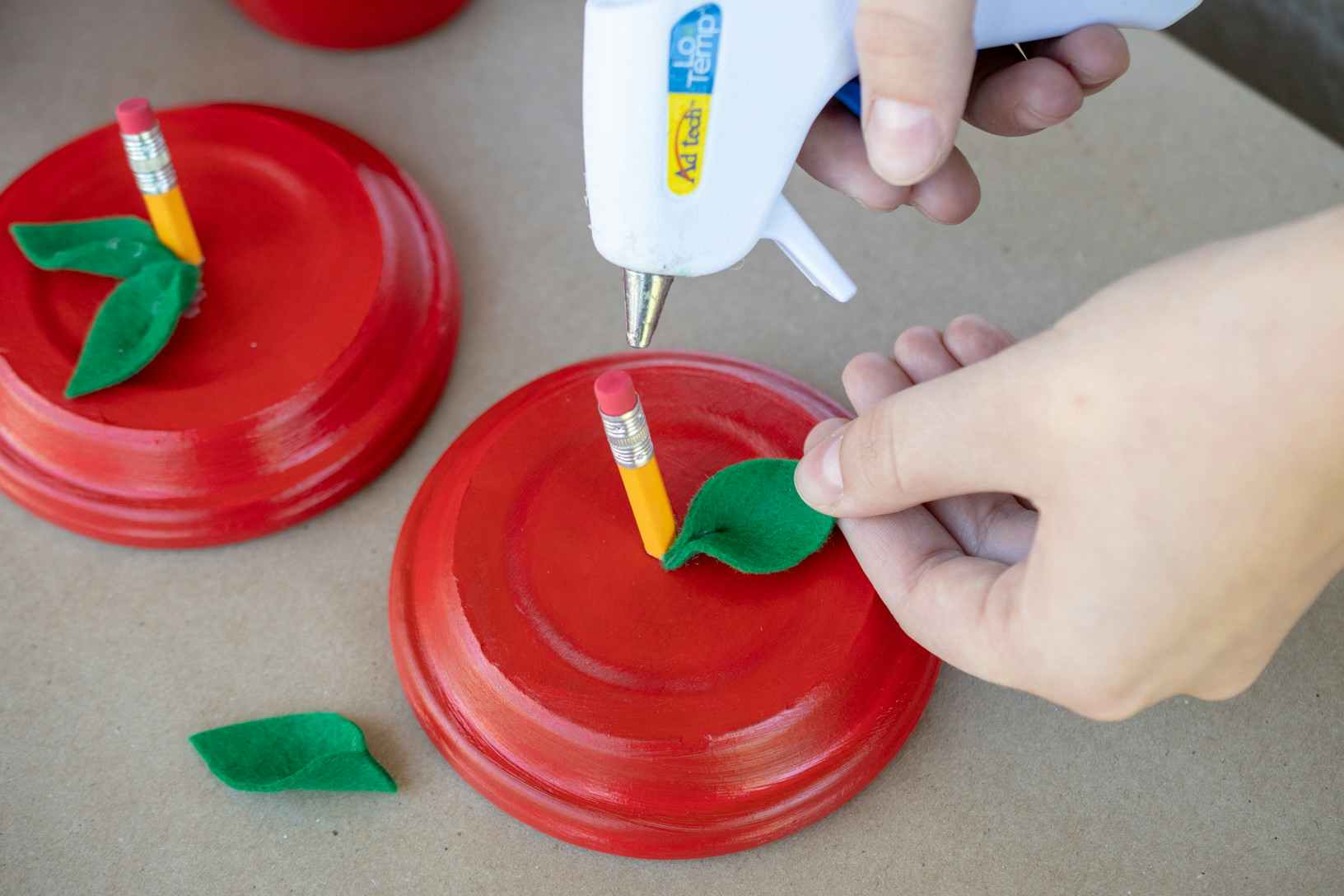 Woman gluing a pencil piece and green felt left onto a red terracotta pot lid.