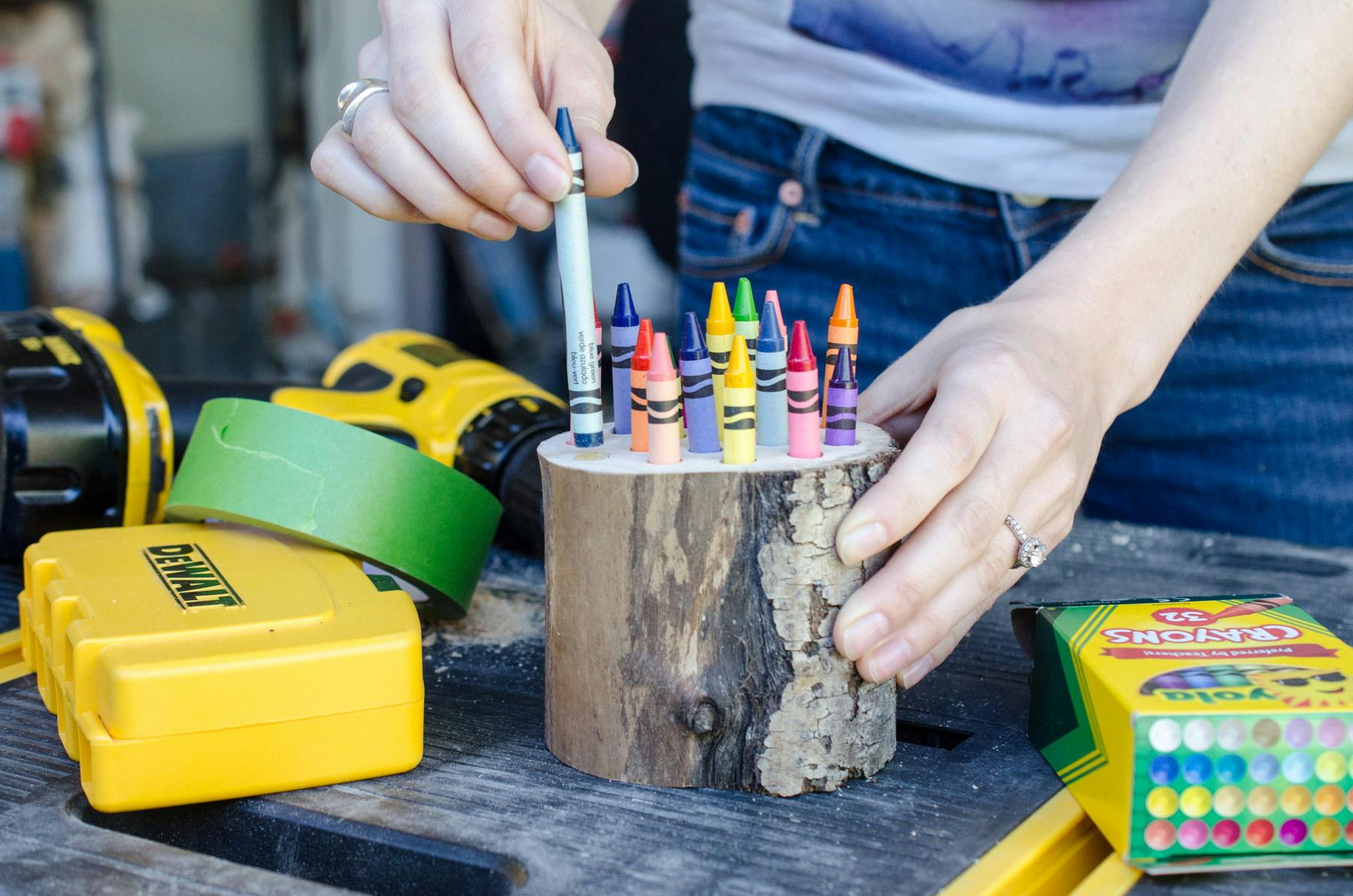 A person placing crayons into a small cut log that has holes in it to hold crayons.