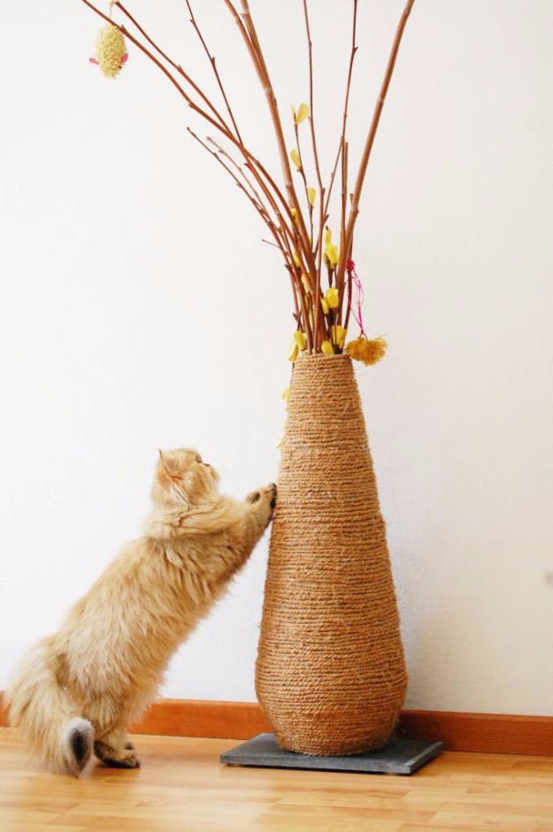 a cat scratching on a large vase covered in rope 