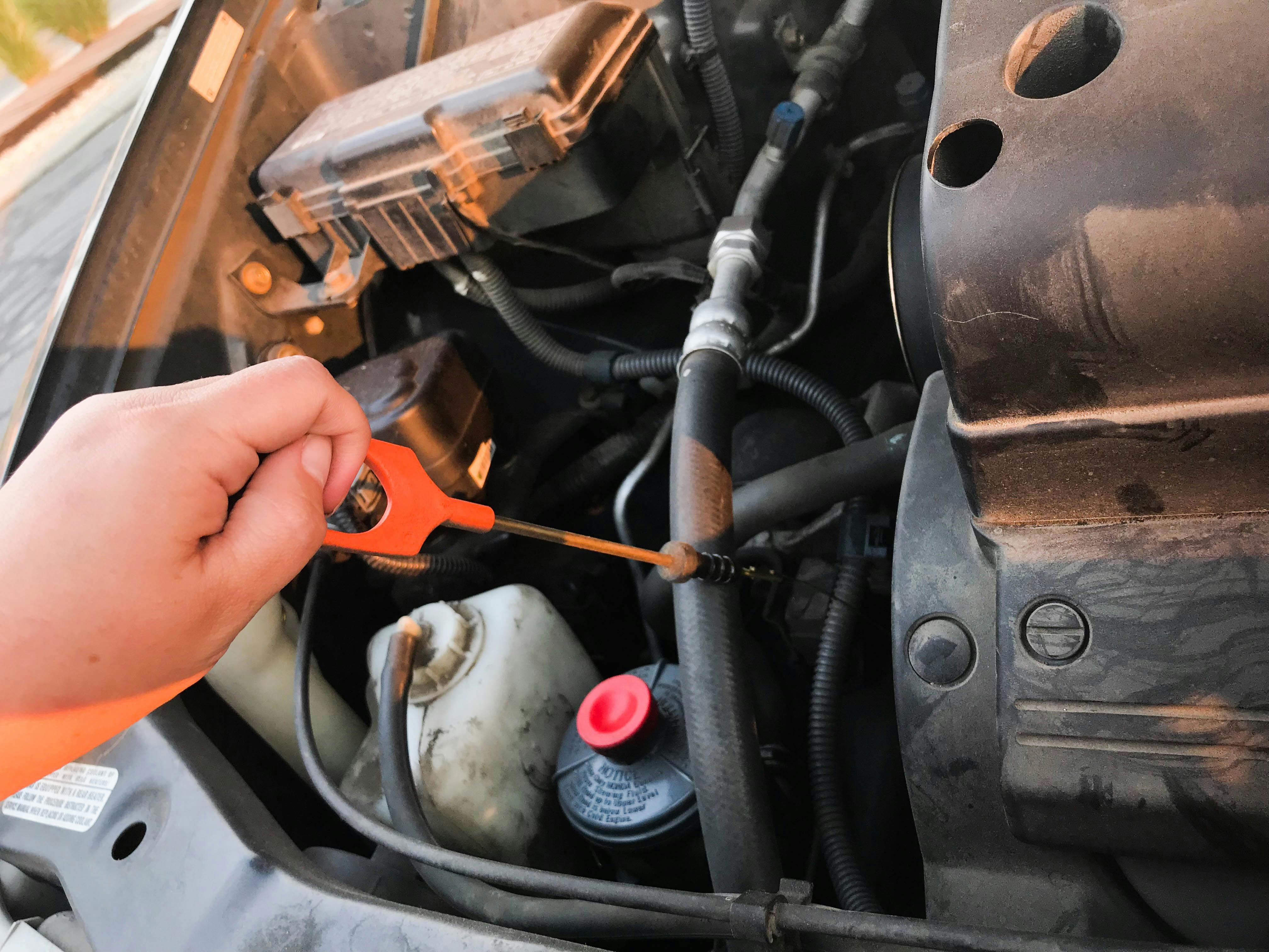 A person checking their car's oil dipstick under the hood.