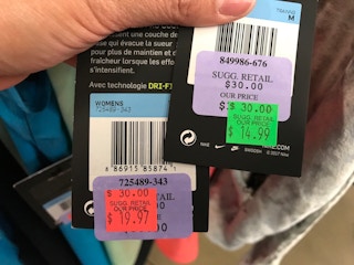 Two Nike tags being held up to show the prices, one with a red clearance sticker, and one with a green clearance sticker.