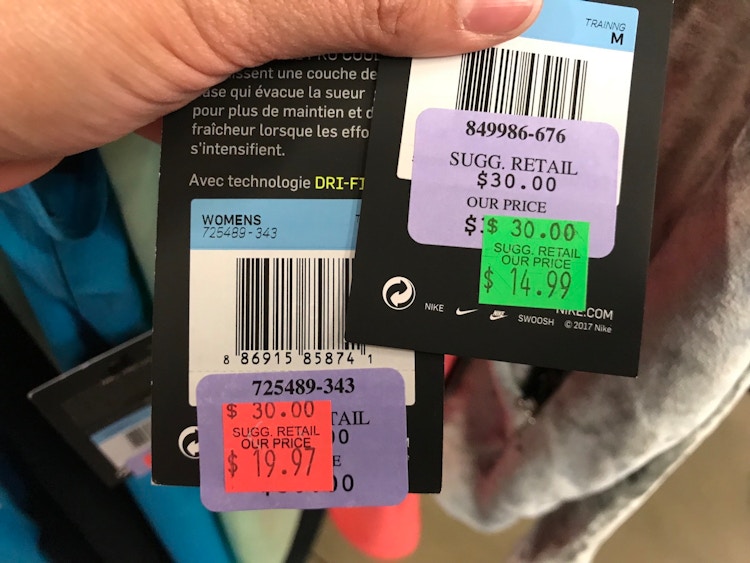 Two Nike tags being held up to show the prices, one with a red clearance sticker, and one with a green clearance sticker.
