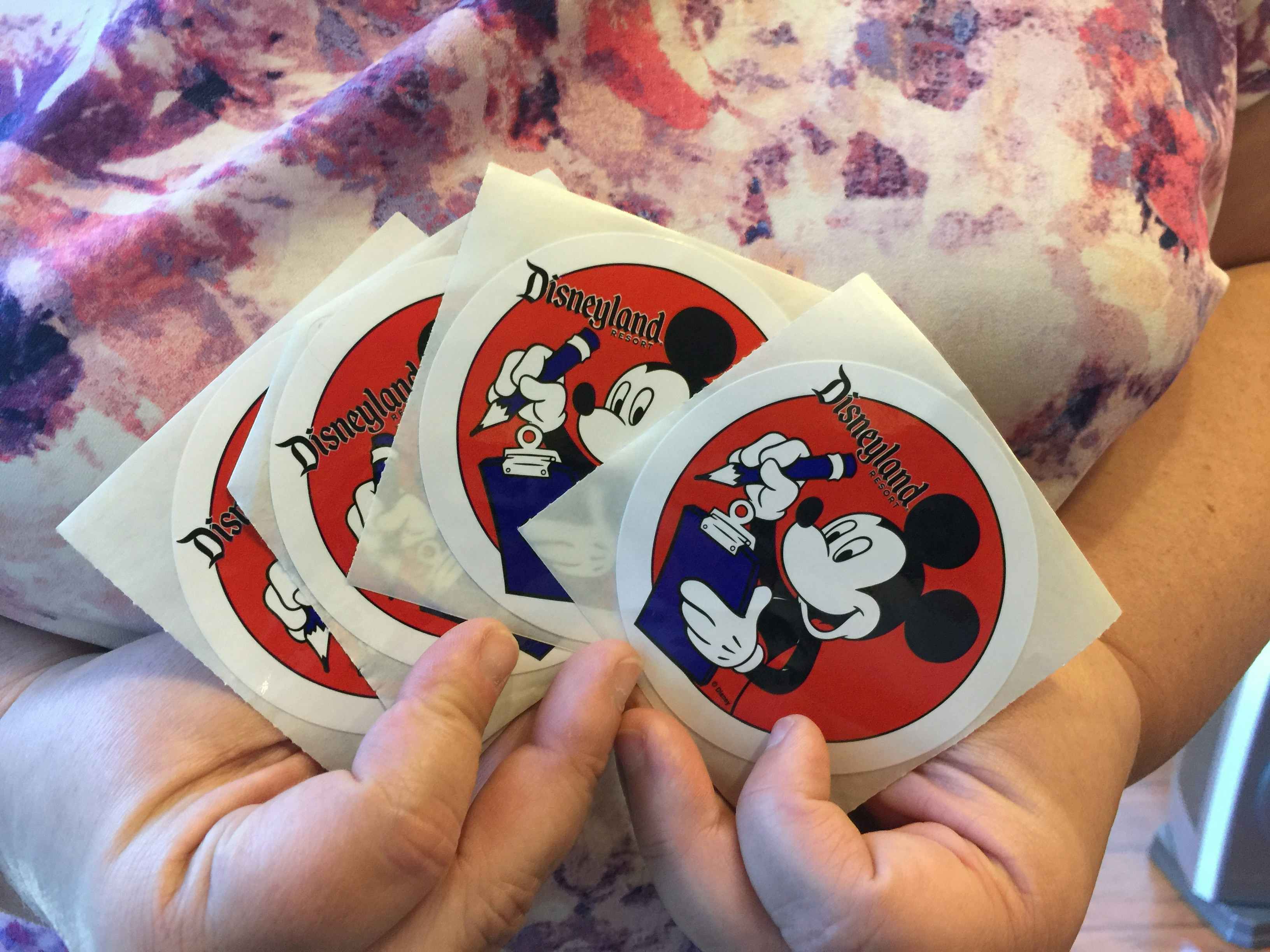 Someone showing off four Disneyland stickers with Mickey Mouse on them.