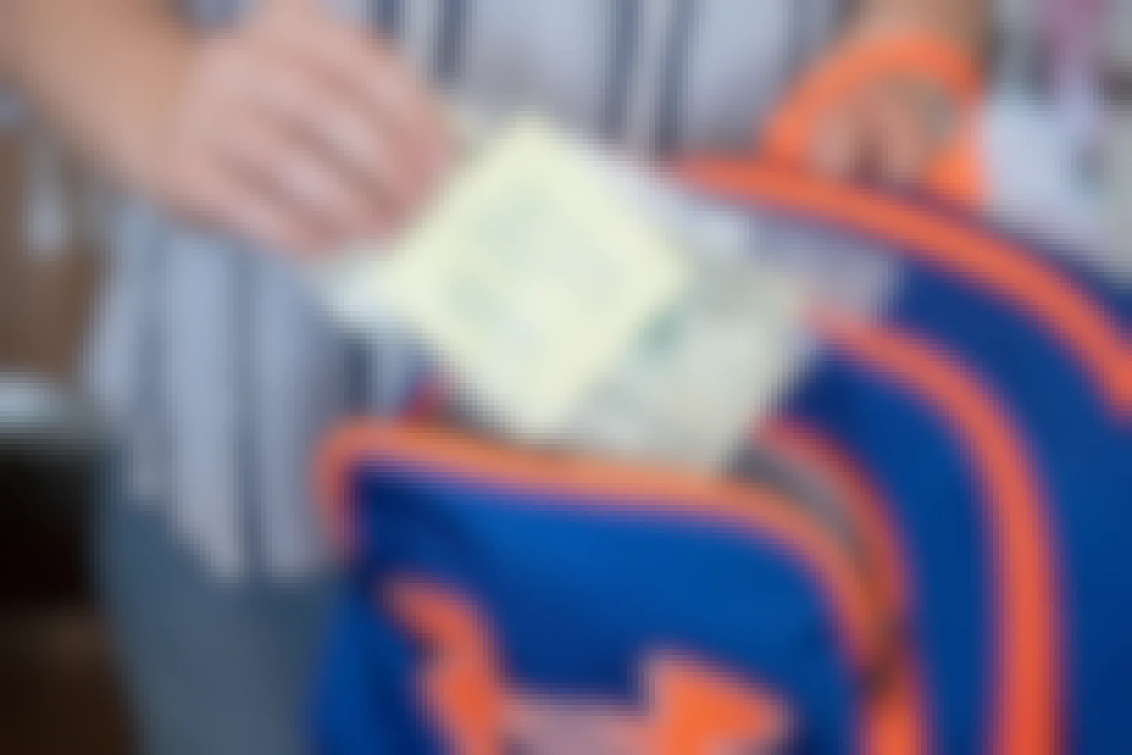Woman placing a Ziploc bag with cash and note that reads "Lunch money to be paid to school. Deliver to front office. Love Mom" into a backpack.