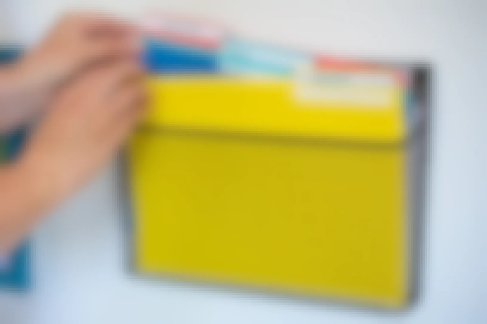 A wall file organizer with bright colored folders and someone reaching to take a blue file.